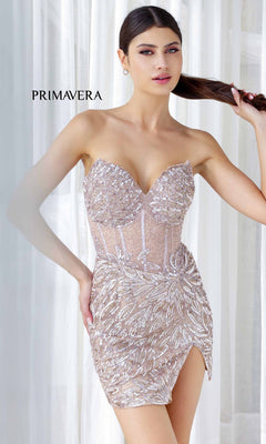 Woman in the Beaded Strapless Mini Hoco Dress: Primavera 4241, a dazzling nude sequin cocktail mini with leafy pattern and high slit, stands before white curtains. The word "Primavera" glows in the background—perfect for any party.