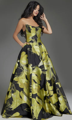 A woman models the strapless Jovani 42435 long prom dress, featuring a bold yellow and black floral design, posed against a gray background—an elegant ball gown ideal for prom or special events.