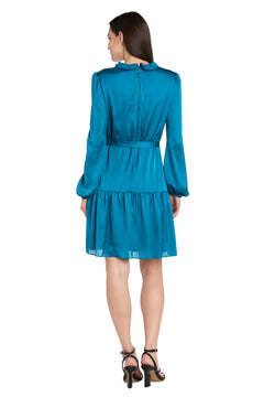 A woman faces away, wearing the R&M Richards 4246 short teal party dress with long sleeves, a ruffled collar, and tiered skirt, styled with black heeled sandals for a chic semi-formal look.