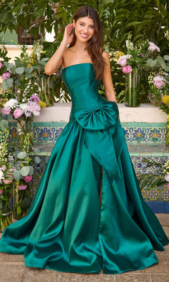 A smiling woman wears an Ava Presley 42477 hunter green strapless prom ball gown featuring a large bow at the waist and a thigh-high slit.