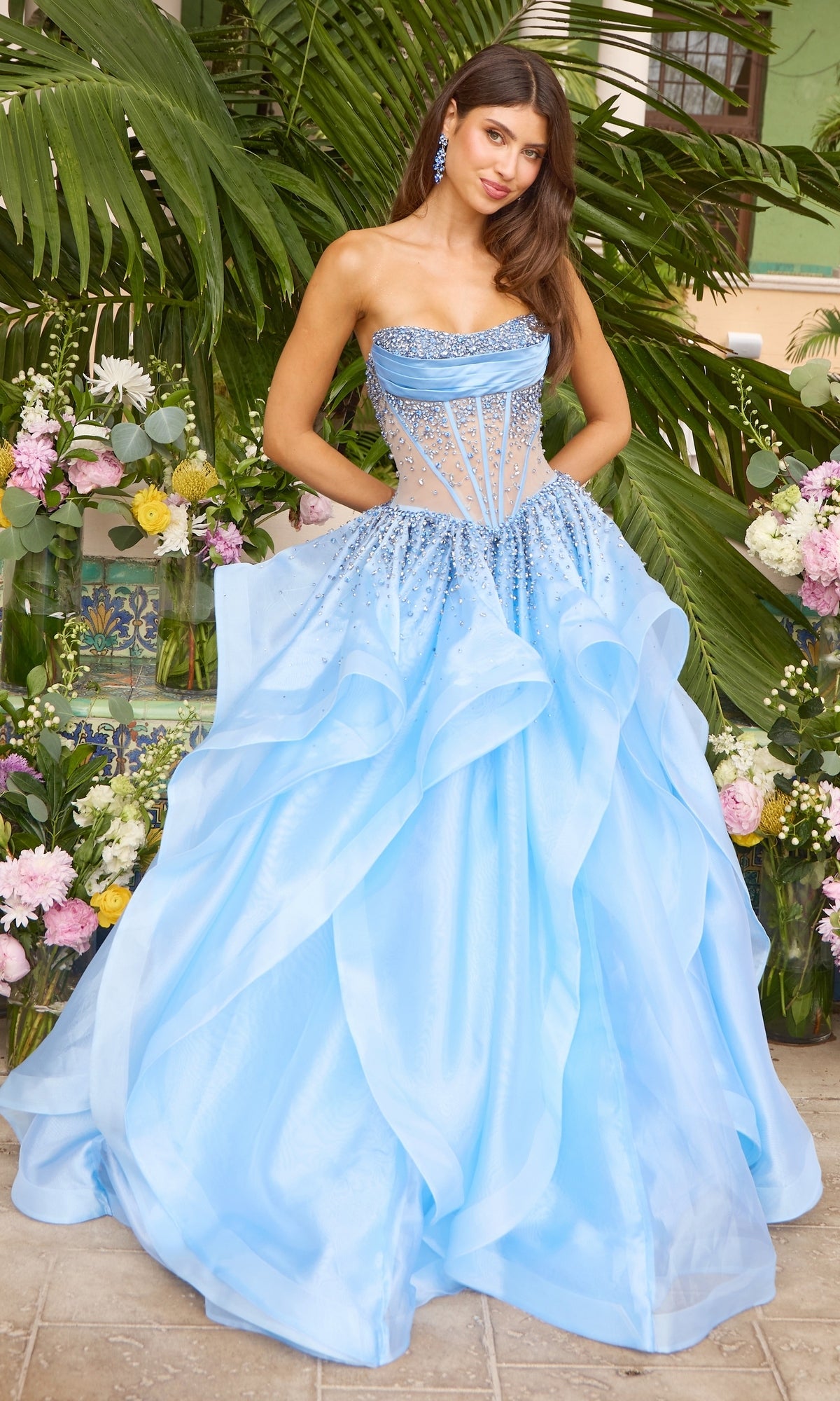 The Ava Presley 42482 is a strapless periwinkle prom dress featuring a beaded, corset-style bodice and a voluminous layered ball gown skirt.
