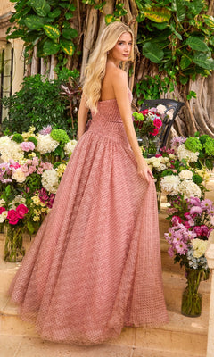 A woman stands on stone steps wearing a floor-length pink Ava Presley 42485 ball gown with a dotted pattern, surrounded by vases of flowers.