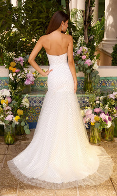 A woman seen from behind wearing an Ava Presley 42489 strapless, floor-length white polka dot prom dress with a small train, standing in front of floral arrangements.