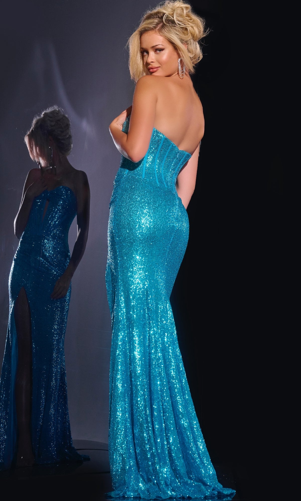 A woman in the Jovani 42514 long prom dress, featuring a strapless sequin design and sweetheart neckline, stands with her back to the camera as her reflection shimmers in a nearby mirror.