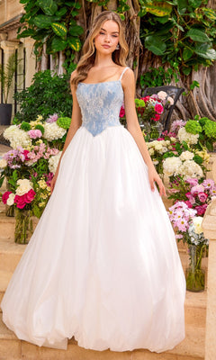 Ava Presley 42519 floor-length gown with a denim blue, lace-overlay corset bodice and a full white skirt, standing among arrangements of flowers.