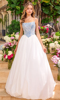 A person stands on stone steps among floral arrangements wearing an Ava Presley 42519 ball gown with a light blue, lace-appliqued bodice and a floor-length white skirt.