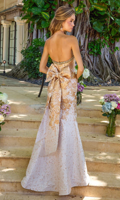 Long Prom Dress: Ava Presley 42535, a strapless white floor-length mermaid gown featuring a metallic gold floral pattern and a large bow at the lower back.