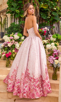 A person wearing a light pink Ava Presley 42540 strapless ballgown with a dark pink floral print on the skirt, standing on stone steps surrounded by flower arrangements.