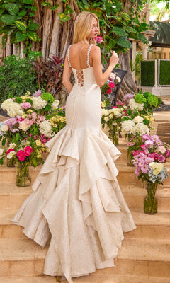 A woman wears a white Ava Presley 42578 gown with pearl-trimmed straps, a lace-up back, and a tiered ruffled skirt while standing among vases of flowers on stone steps.