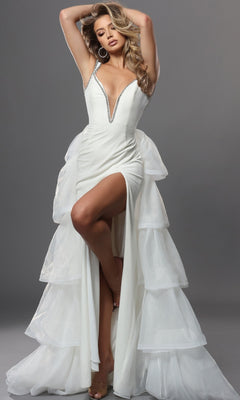 An elegant woman poses with arms raised against a gray background, wearing the off-white Jovani 42661 long formal dress featuring a sleeveless design, deep V neckline, tiered tulle ruffles, high slit, and shimmering silver trim.