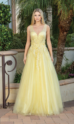 A woman poses gracefully outdoors in the Backless Glitter Tulle Ball Gown Prom Dress 4272, a sleeveless, floor-length yellow gown with elegant details, surrounded by lush greenery and a palm tree.