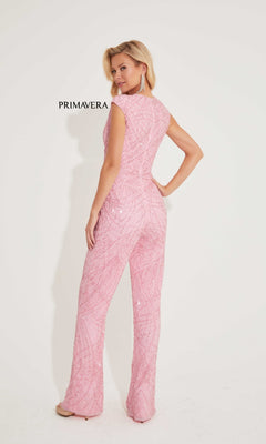 A woman faces away, wearing the Long Formal Jumpsuit 4275 by Primavera in pink sequin beads, set against a plain white background with "PRIMAVERA" on the wall.