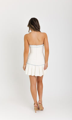 A woman faces away from the camera, wearing the Ava Presley 42928 Strapless Tweed Mini Dress with a pleated skirt and beige high heels, posed against a plain white background.