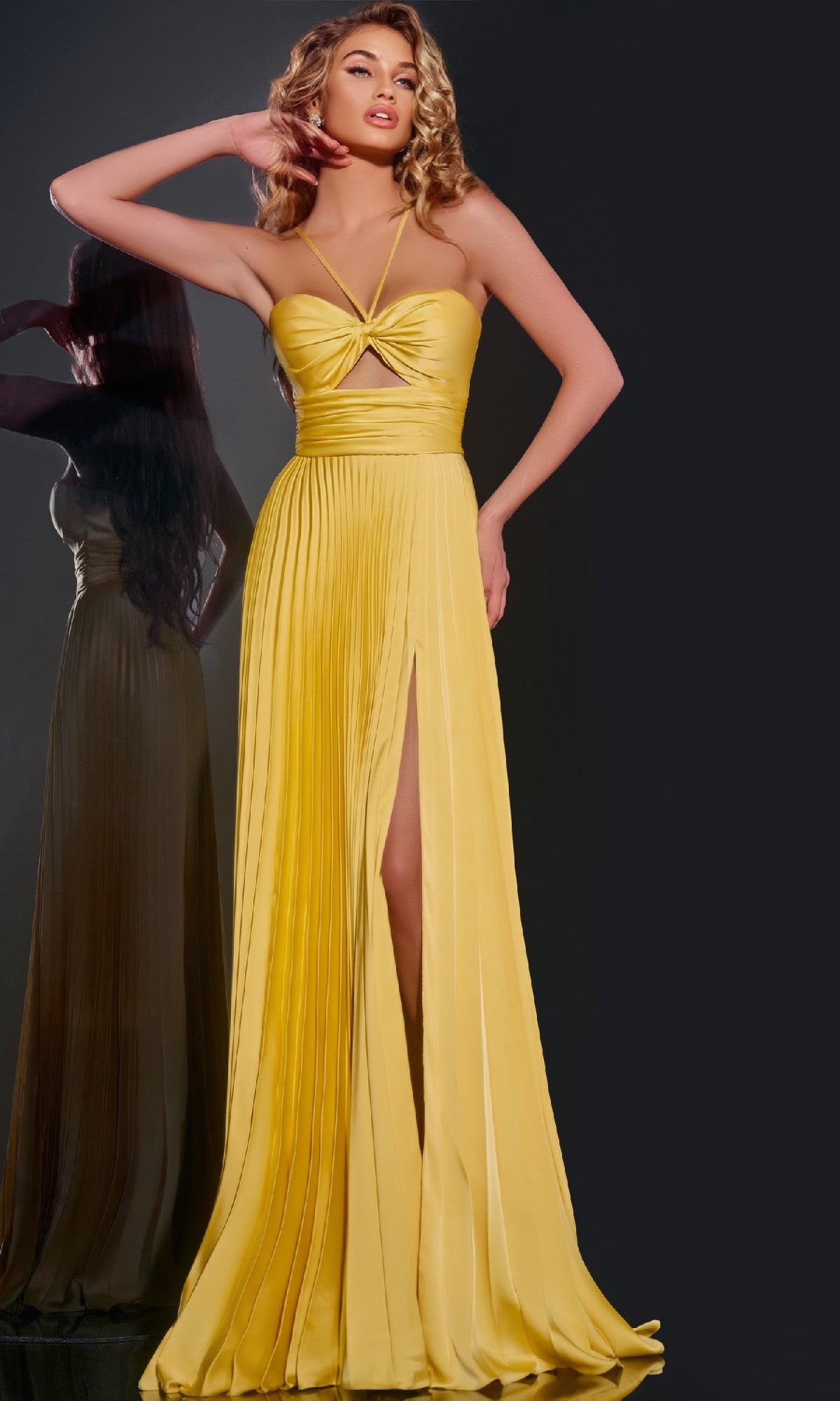 Woman wearing the Long Prom Dress: Jovani 42971—a strapless yellow pleated A-line gown with sweetheart neckline, front slit, and midriff cutout—poses against a dark background with her reflection visible beside her.