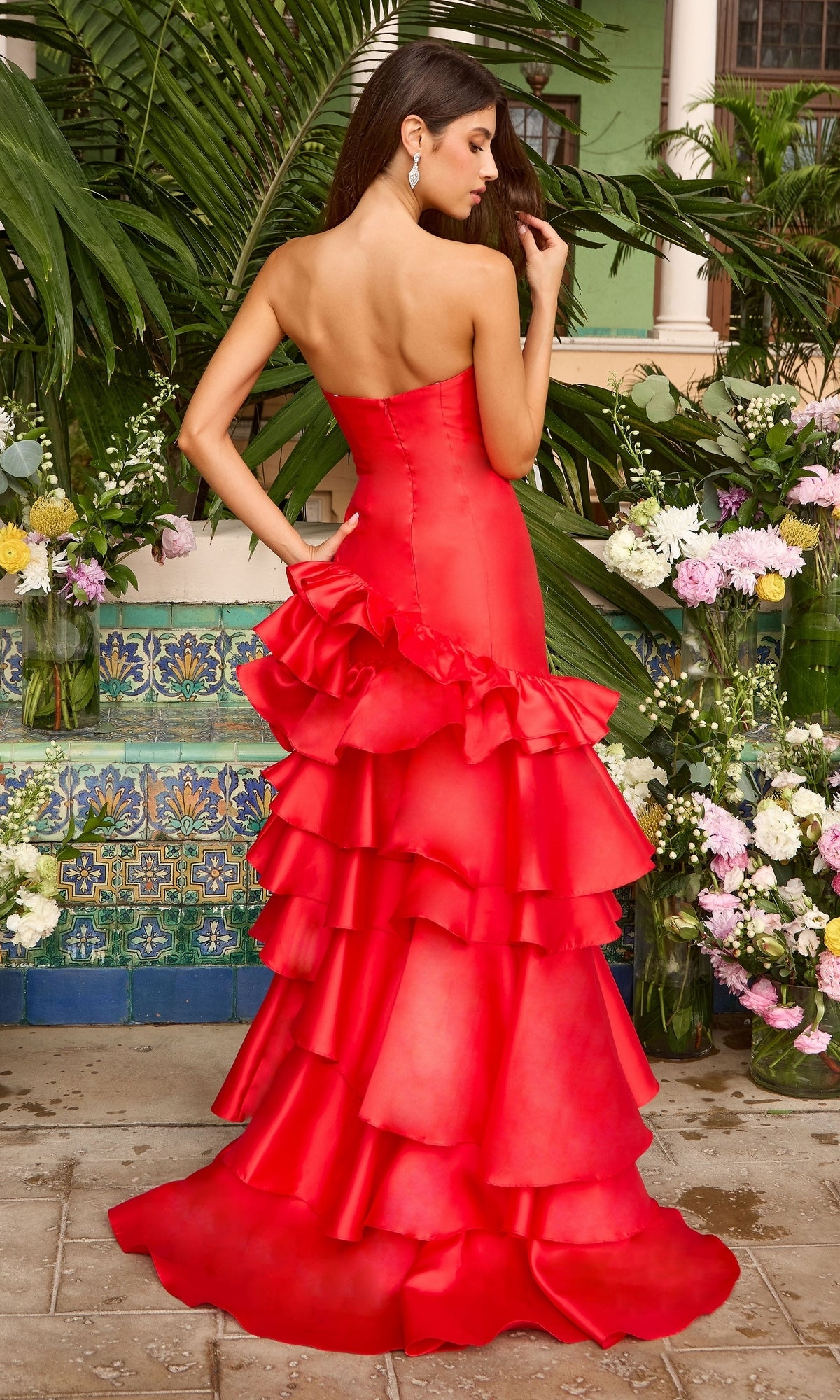 A woman wearing an Ava Presley 43015 long prom dress, a strapless red floor-length gown with an asymmetrical tiered ruffled skirt.