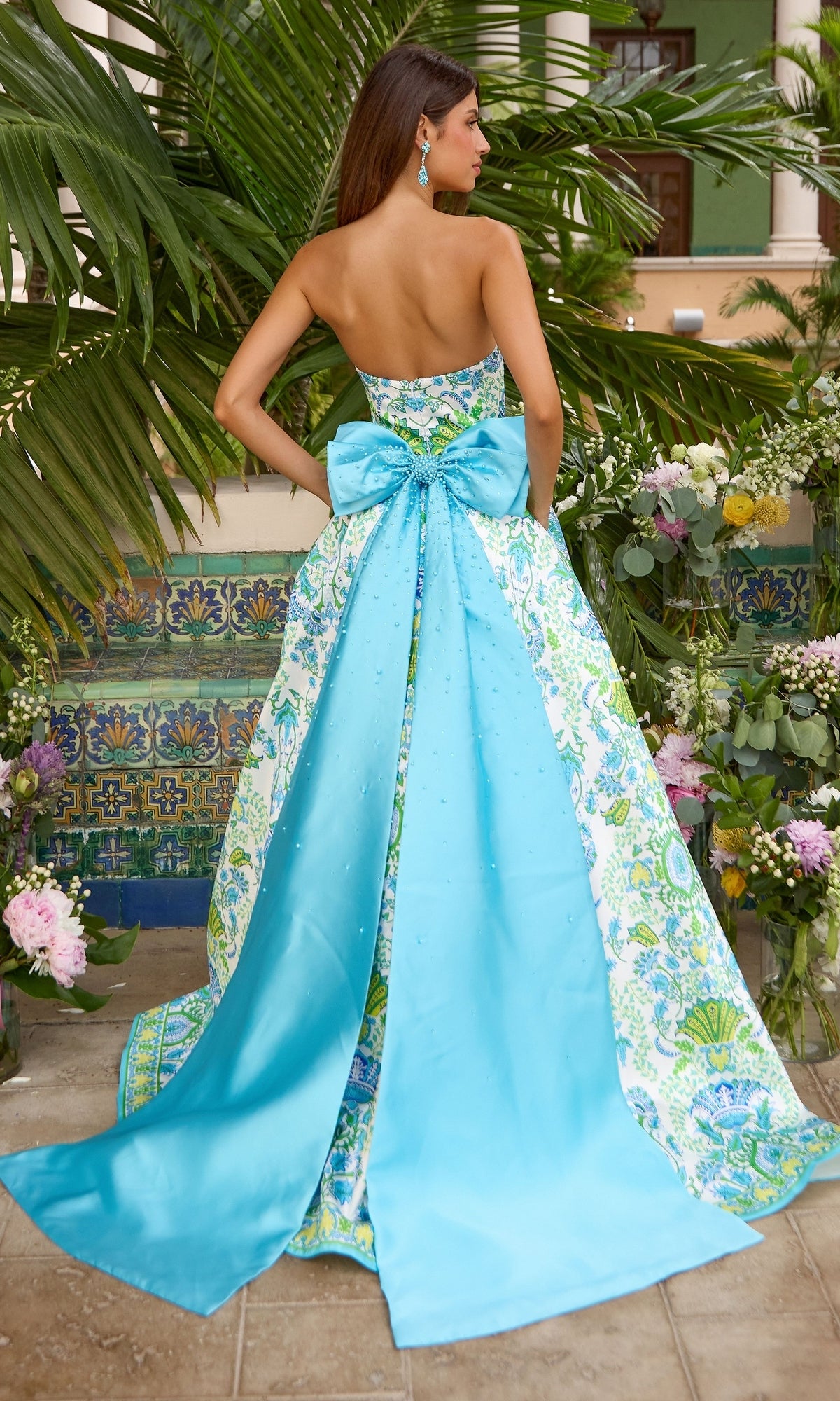 Ava Presley 43017 strapless floor-length prom ball gown with a blue and green floral pattern, a large blue bow at the waist, and a long, flowing train.