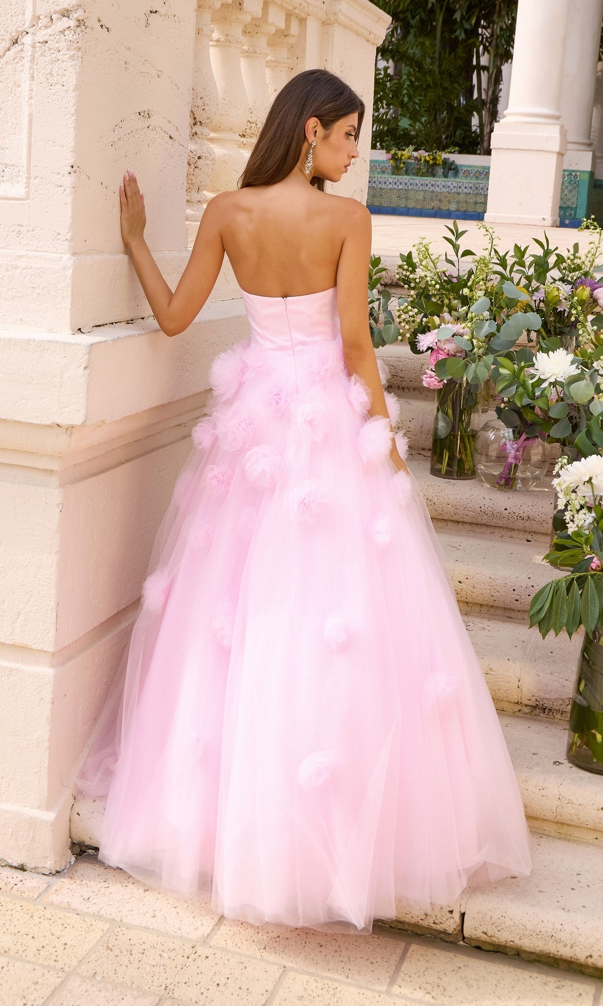 Woman standing on stone steps wearing a light pink Ava Presley 43019 strapless, floor-length gown adorned with 3D floral appliqués.