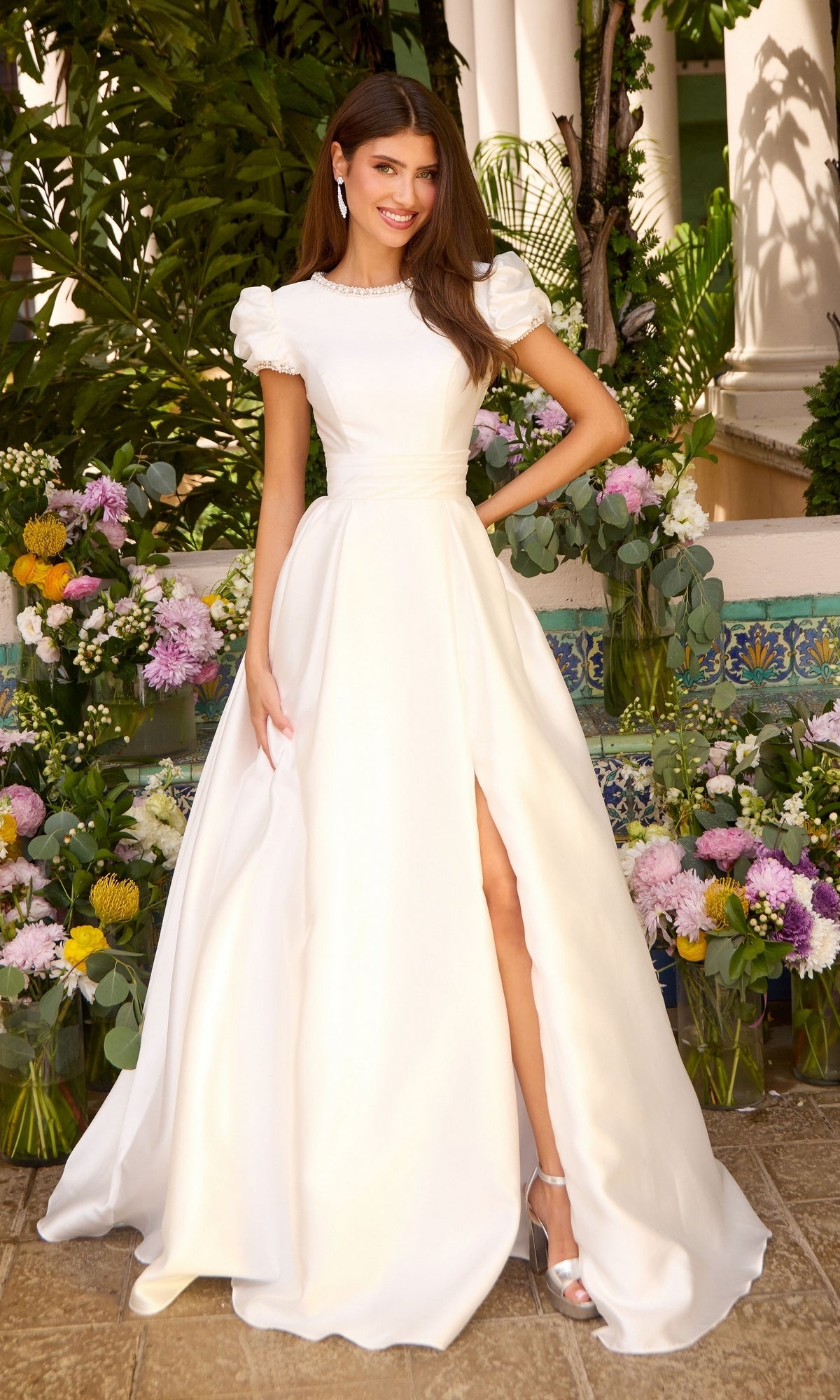 Woman wearing a floor-length white puff sleeve Ava Presley 43023 prom dress with a high neckline and a front slit.