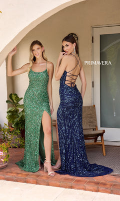 Two women pose outside; one stuns in the Primavera 4303 Backless Long Sequin Prom Dress in green with a thigh-high slit, while the other dazzles in a navy strappy-back evening gown. "PRIMAVERA" is displayed on the wall behind them.