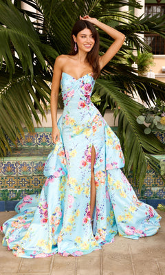 A woman wears an Aqua Multi Ava Presley 43039 long prom dress, featuring a light blue strapless floral design with a floor-length overskirt and a high thigh slit.
