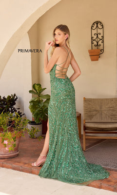 A woman poses outdoors by potted plants and a wooden chair, wearing the Primavera 4303 Backless Long Sequin Prom Dress in green with a strappy back, standing against a stucco wall.