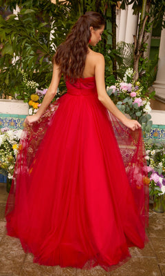 A person stands in a garden wearing an Ava Presley 43045 strapless, floor-length red gown with a full tulle skirt.