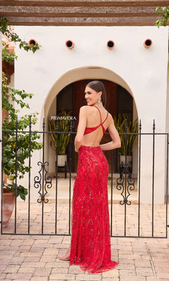 A woman stands outdoors by a gate, smiling over her shoulder in the Primavera 4316 Open-Sides Long Sequin Prom Dress, featuring thin straps and a chic strappy-back design.