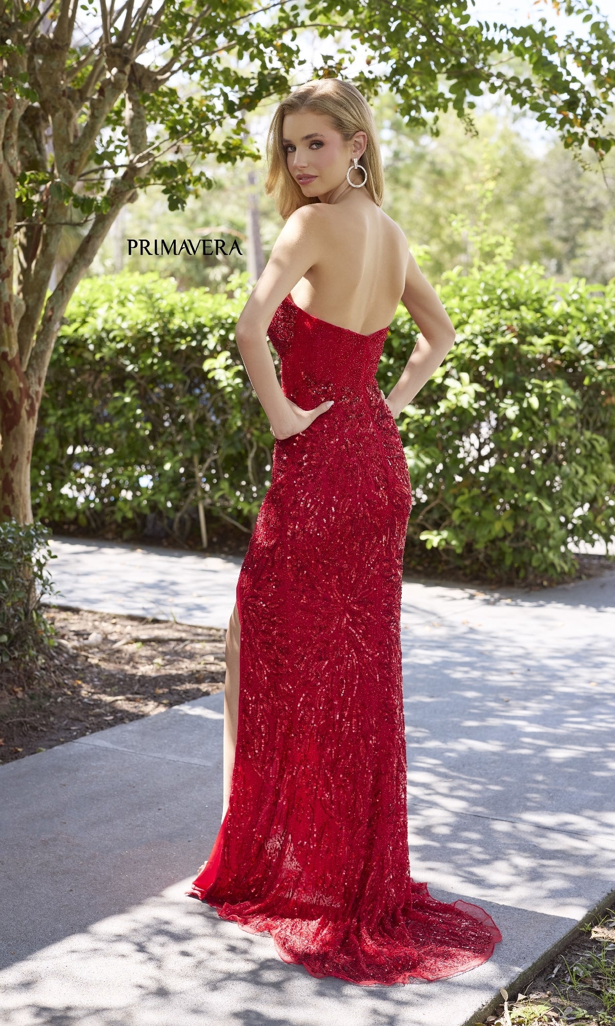 A woman stands outdoors on a path surrounded by lush greenery, wearing the Primavera 4321 strapless long sequin prom dress featuring a sweetheart neckline.