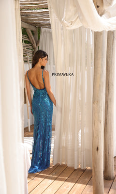 A woman wears the Primavera 4325 open-back long sequin prom dress in blue, standing on a wooden deck between white curtains under a rustic canopy. "PRIMAVERA" is displayed in the background.