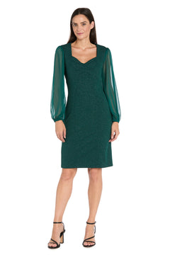 Woman wearing a knee-length green glitter sheath dress with sheer long sleeves on a white background