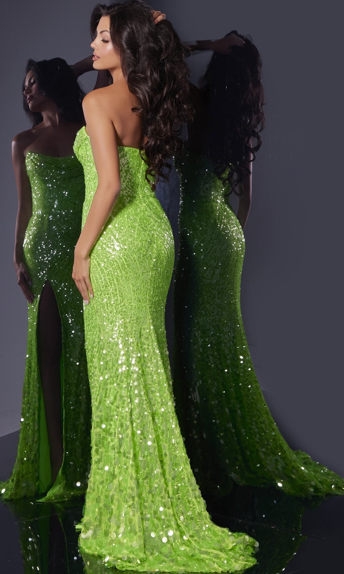 A woman models the Long Prom Dress: Jovani 43338—an elegant, bright green, strapless sequin gown with a high slit—posing before a mirror to showcase both its back and side views.