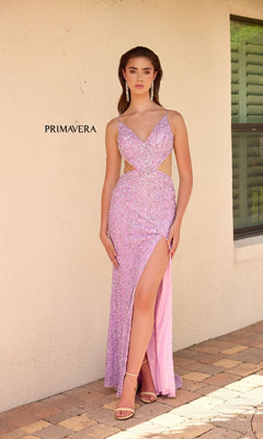 A woman in the Primavera 4334 long prom dress, featuring sparkly light purple sequins, side cut-outs, and a thigh-high slit, stands on a brick patio by a beige wall and window.