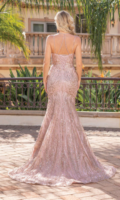 Wearing the Long Glitter Mermaid Formal Prom Dress 4337, a woman stands outdoors with her back to the camera. The light pink, floor-length gown shimmers in the sunlight by a wrought iron railing and tropical plants, exuding elegance.