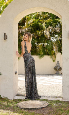 A woman wears the sparkly, floor-length Primavera 4344 long prom dress, standing under a stone archway with lush greenery and a statue in the background. "PRIMAVERA" is displayed.