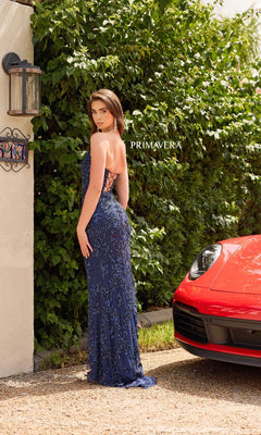 A woman in the Strapless Long Sequin Prom Dress: Primavera 4347 stands outdoors by greenery and a red sports car, facing away with her head turned to the camera. "PRIMAVERA" appears in the background, emphasizing this eye-catching formal look.