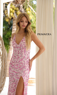 Wearing the Long Prom Dress: Primavera 4348, a woman stands outdoors by a palm tree. Her fitted pink gown features an open back, thigh-high slit, shimmering sequins, and hot stone embellishments beneath "PRIMAVERA" signage.