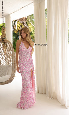 A woman in the Primavera 4348 Long Prom Dress—a fitted light pink sequin gown with hot stone embellishments and a high slit—stands indoors by white curtains and a hanging chair. "PRIMAVERA" is displayed on the curtain.