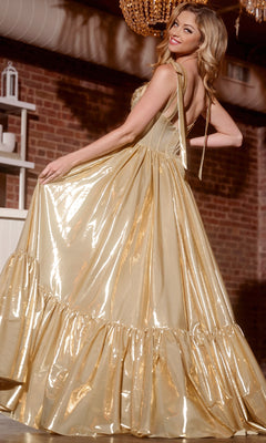A woman poses indoors in front of a brick wall, looking over her shoulder and holding the skirt of the shiny gold Jovani 43596 long prom dress, featuring a corset bodice and ruffled hem.