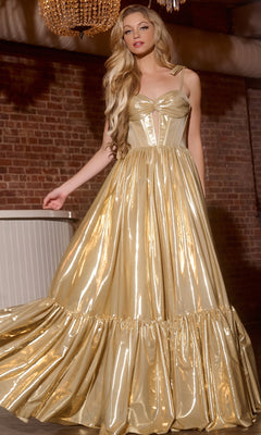 A woman poses indoors against an exposed brick wall wearing the Jovani 43596 long prom dress, featuring a shiny metallic gold finish, corset bodice, and full skirt.