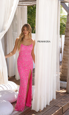 A woman in the Strappy Long Beaded Prom Dress: Primavera 4359, bright pink with a thigh-high slit, stands on a wooden deck between white curtains. "PRIMAVERA" appears on the curtain behind her.