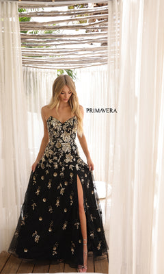 A woman wearing the Strapless Beaded Long Prom Dress: Primavera 4361, featuring gold floral embroidery and a thigh-high slit, stands under a pergola with sheer curtains. "PRIMAVERA" appears in the background.