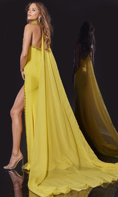 A woman in the Jovani 43658 long formal dress, featuring a yellow hue, beaded cape, and high slit, stands on a glossy surface facing away, her shimmering reflection visible behind her.