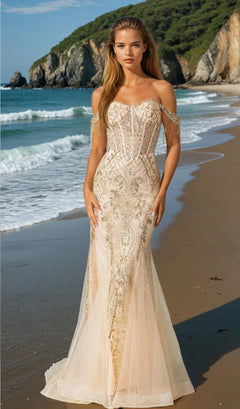 A woman stands on a beach in the Fringe Long Glitter Prom Dress (Dancing Queen 4365), featuring an off-the-shoulder design, fitted beaded corset bodice, sheer panels, with ocean waves and cliffs behind her.