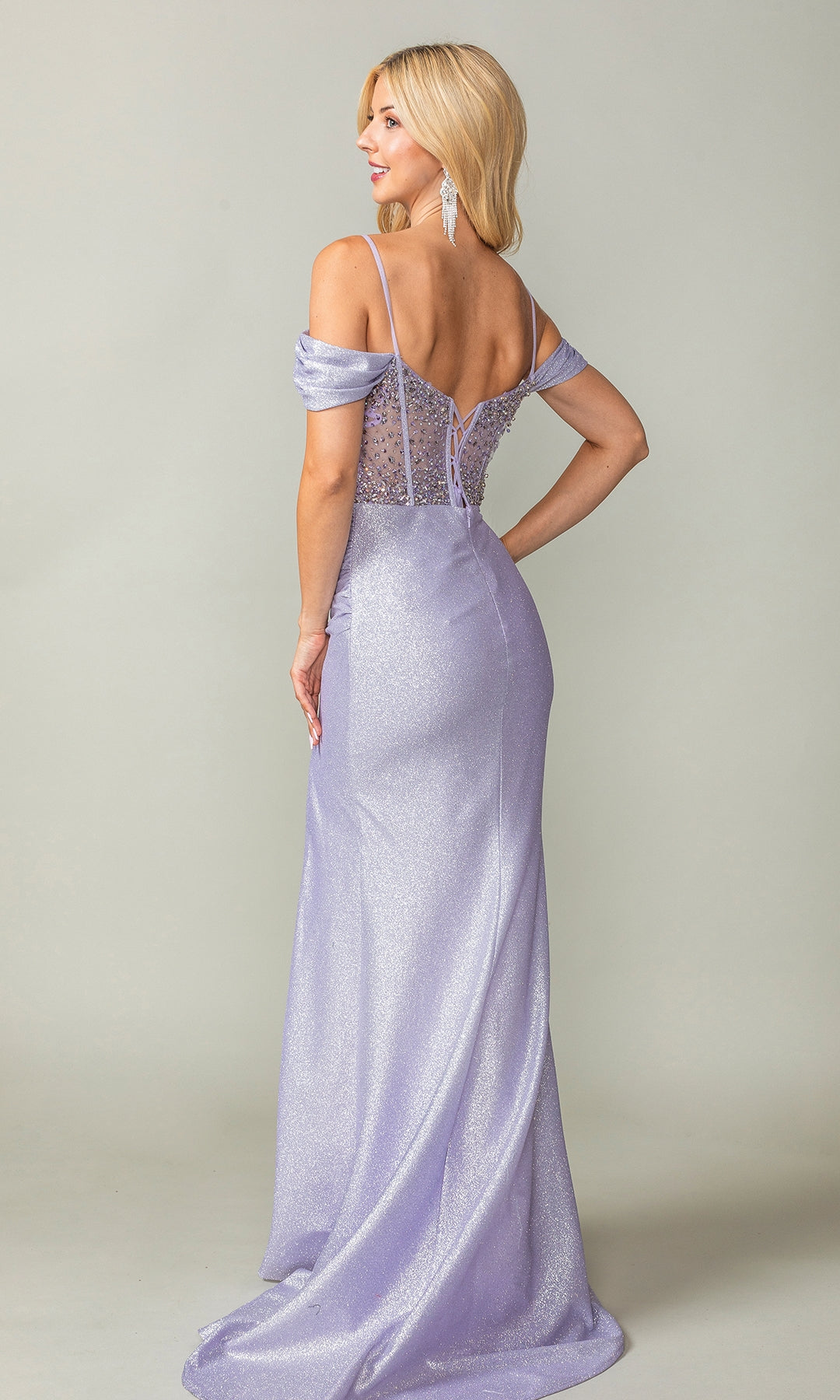 A woman stands with her back to the camera, wearing the Beaded-Corset Long Prom Dress (Dancing Queen 4367)—a light purple, off-the-shoulder gown with a fitted bodice, sheer details, and a small train.