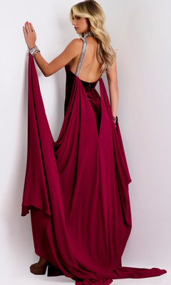 A woman wearing the Jovani 43699 long prom dress—featuring a backless velvet halter design with draped fabric and a high-leg slit—stands against a white background, facing away from the camera.