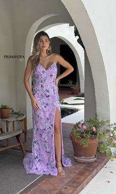 Wearing the Primavera 4374 long prom dress, a woman stands under an arched patio surrounded by potted plants and outdoor furniture.