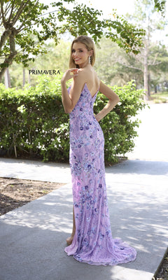 A woman poses and smiles outdoors in the Primavera 4374 long prom dress, featuring a strapless design with lilac floral embroidery and embellishments.