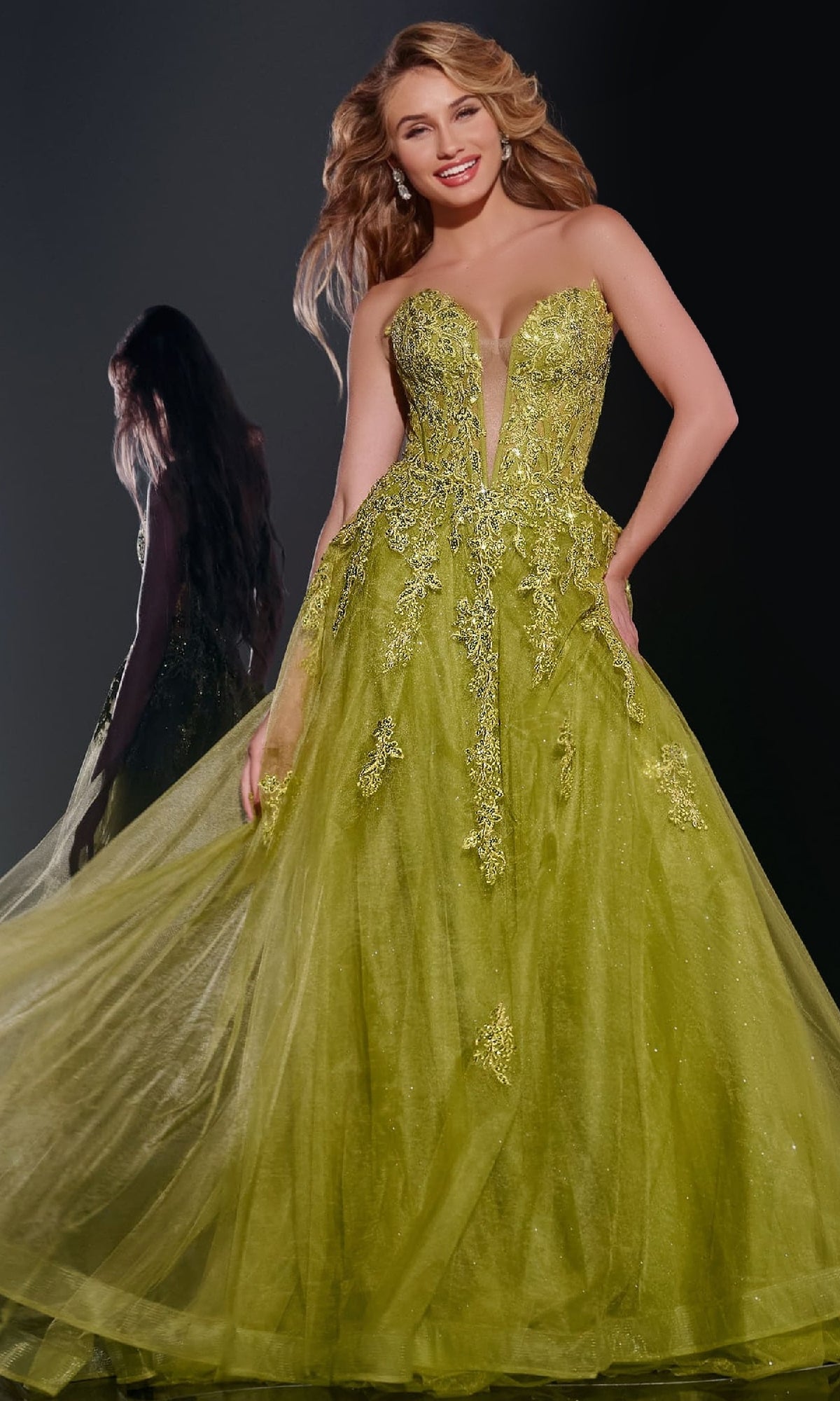 A woman models the Jovani 43849 long prom dress, featuring a strapless, bright green glitter tulle design with embellishments, while a back view of the gown is shown in the background.