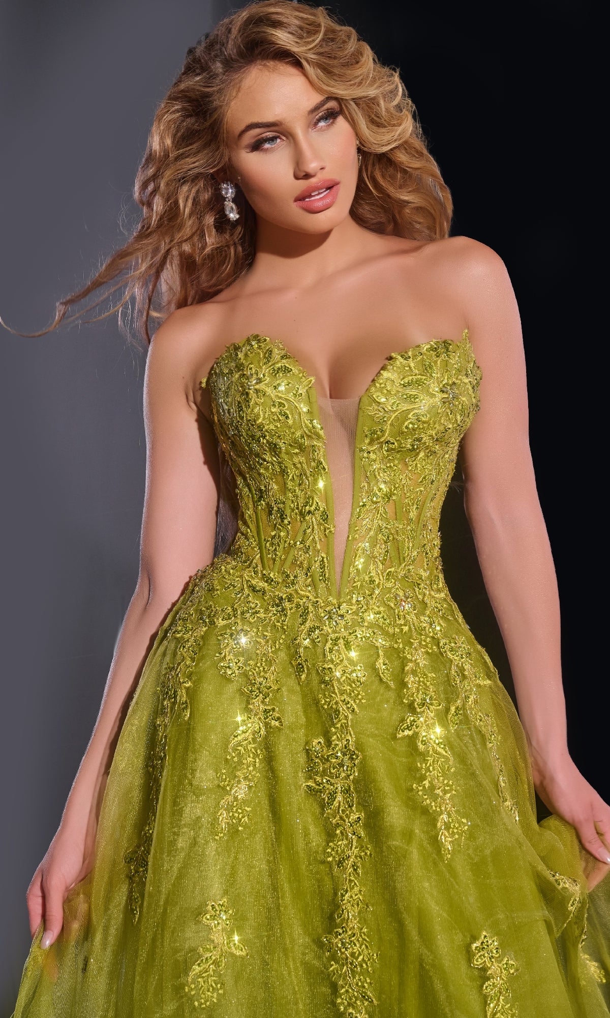 A woman poses in the Jovani 43849 Long Prom Dress, a strapless lime green ball gown with intricate floral details and elegant lace embroidery, set against a dark background.
