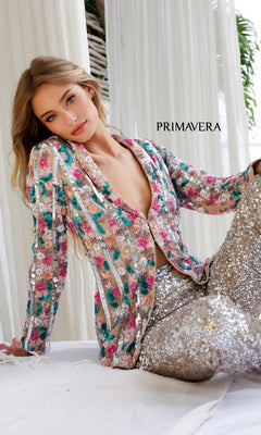 A woman wearing the Primavera 4388 Long Sequin Formal Jumpsuit sits on a white surface with white curtains and greenery behind her. The word "PRIMAVERA" is displayed beside her.